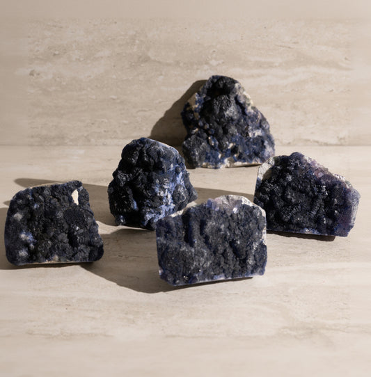 Five dark purple crystal rocks on a beige surface