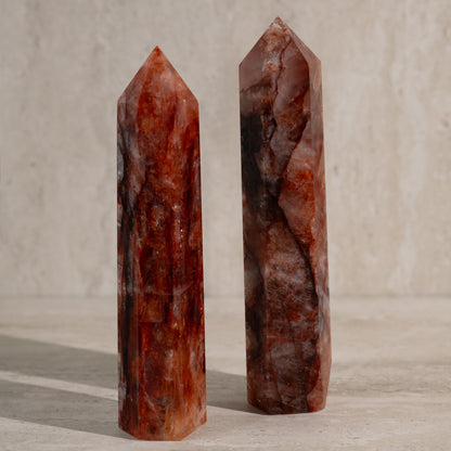 Two polished red crystals on a wooden surface with a neutral background