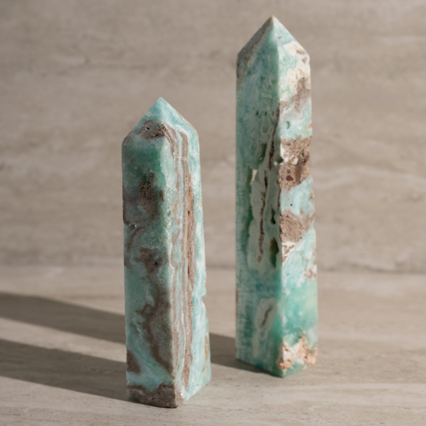 Two turquoise crystal obelisks on a wooden surface with a neutral background