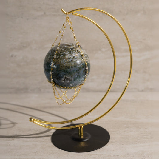 Decorative piece with a gold crescent moon stand holding a stone and chain on a wooden surface.