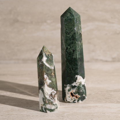 Two green crystal points on a wooden surface with a neutral background