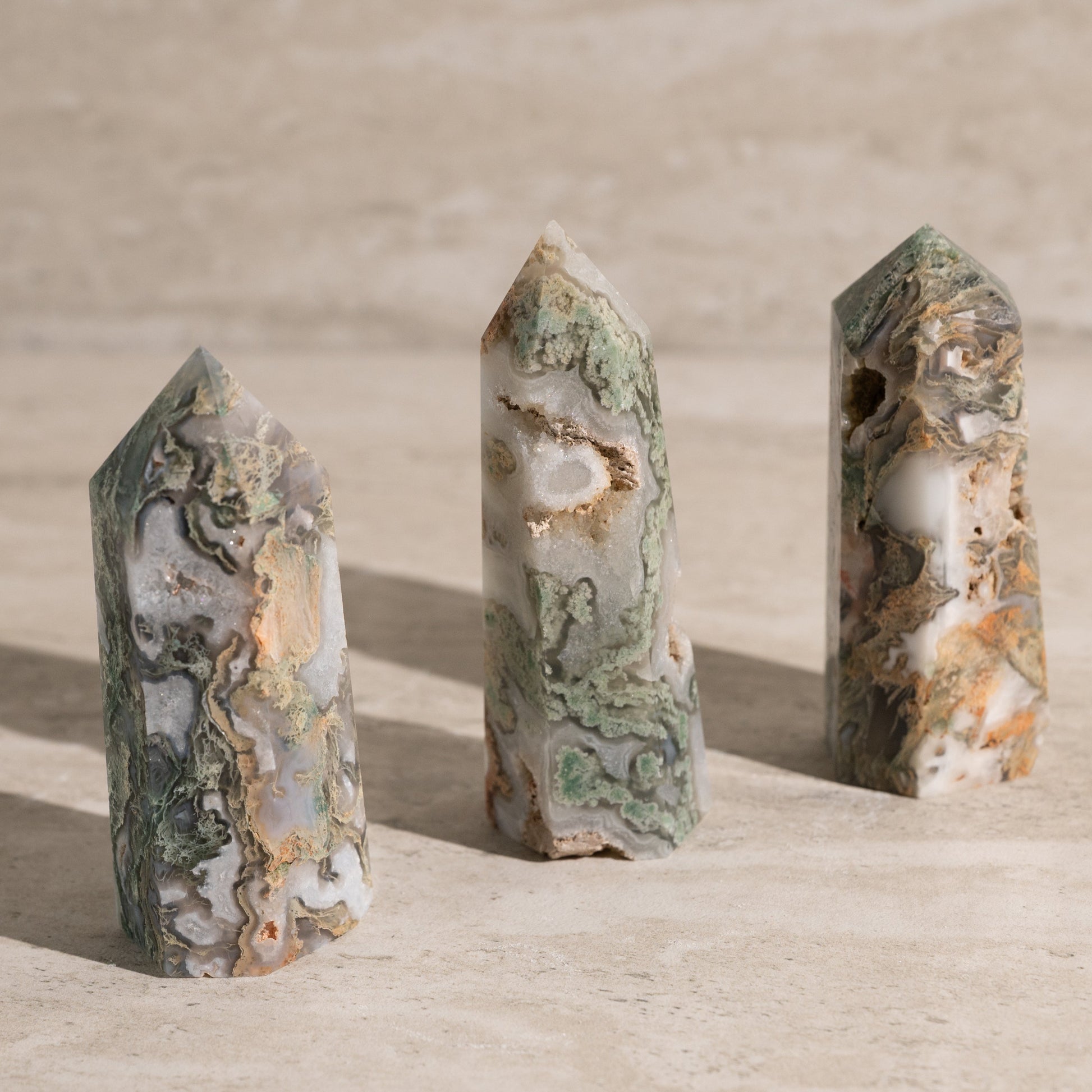 Three green and brown crystal points on a beige surface