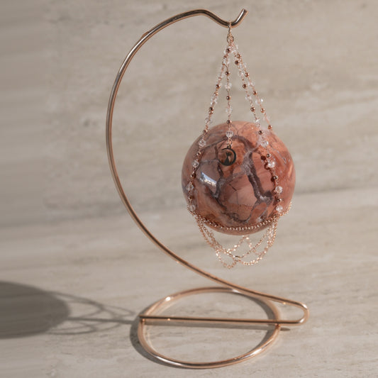 Decorative item with a pink stone and beaded chain on a metal stand against a neutral background