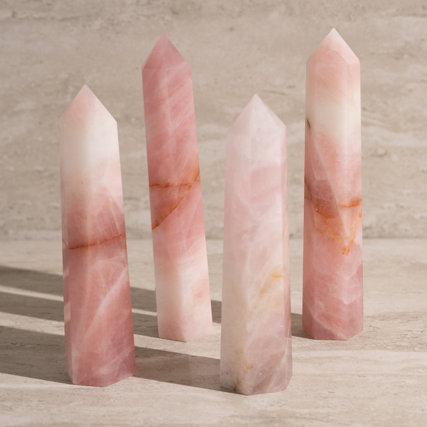 Four pink crystal sticks on a wooden surface with a neutral background