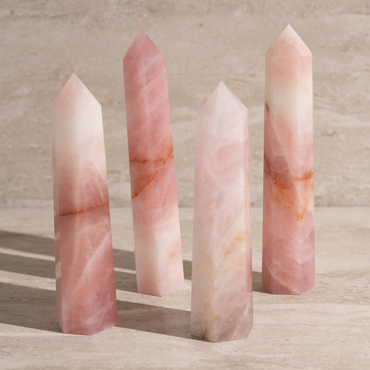 Four pink crystal sticks on a wooden surface with a neutral background