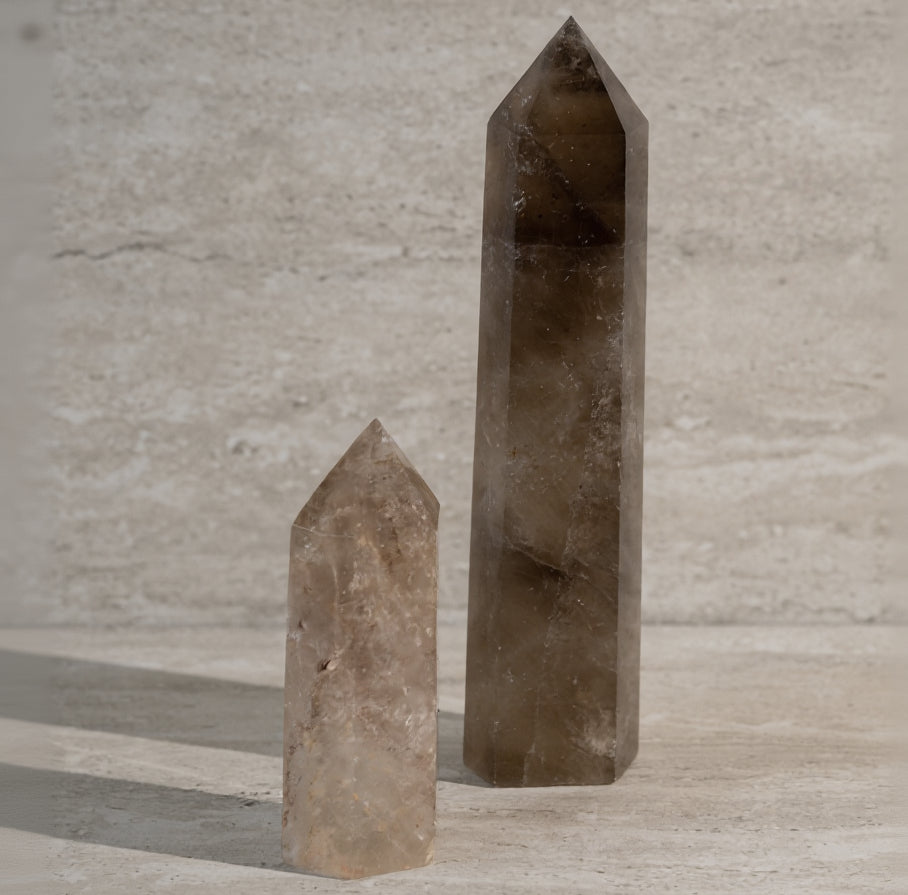 Two brown crystal obelisks on a light wooden surface with a neutral background