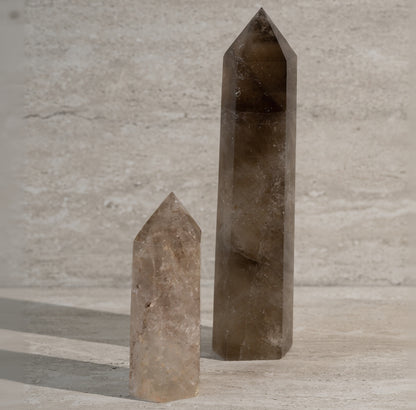 Two brown crystal obelisks on a light wooden surface with a neutral background
